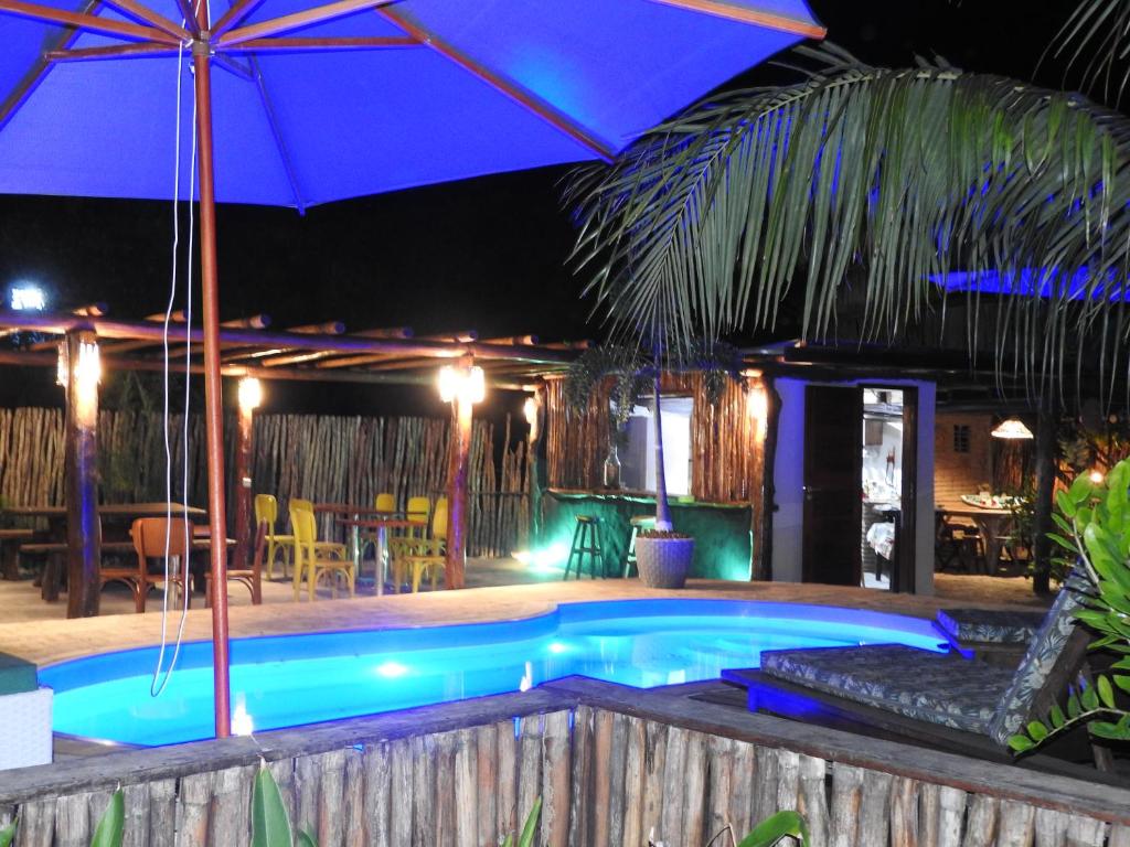 a swimming pool with an umbrella and tables and chairs at Pousada Santa Aldeia in Barra Grande