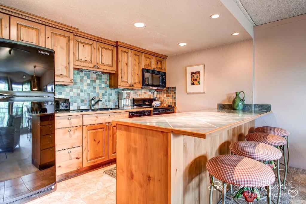 una cocina con armarios de madera y una gran isla con taburetes. en Impeccable Ski In Ski Out Unit with Mountain Views from Private Balcony, Steps From Downtown TE402 en Breckenridge