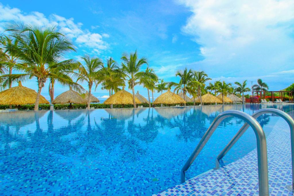 a swimming pool with palm trees and straw huts at Apartasuites Samaria - Club de Playa in Santa Marta