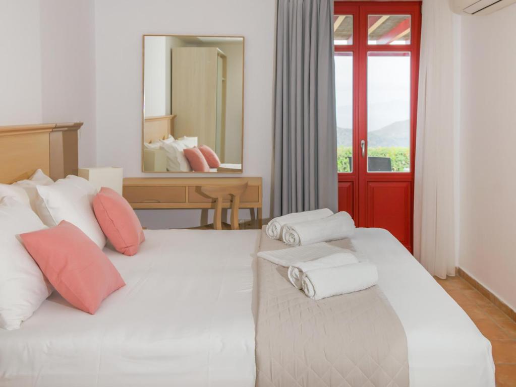 a bedroom with a white bed with pillows and a mirror at Bella Resorts Andros in Andros