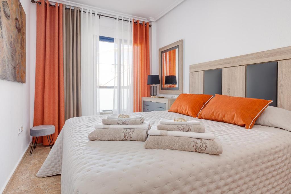 a bedroom with a large white bed with orange accents at Penthouse Naomi with two terraces, private solarium, sea view, swimming pool, with underground parking, pets allowed in Orihuela Costa