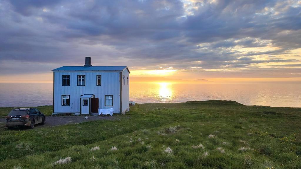 a white house with a car in front of the ocean at Happy-Cove Guesthouse - by the sea in Bakkafjörður