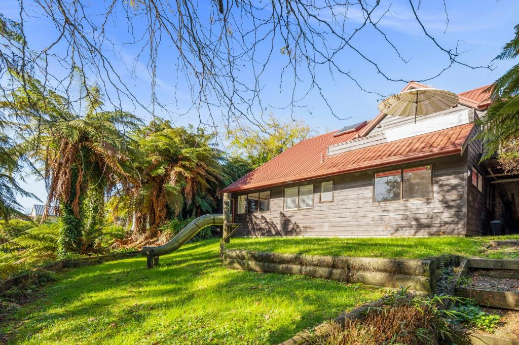 an old house with a red roof on a green yard at Bushland Retreat - Rotorua Holiday Home in Koutu