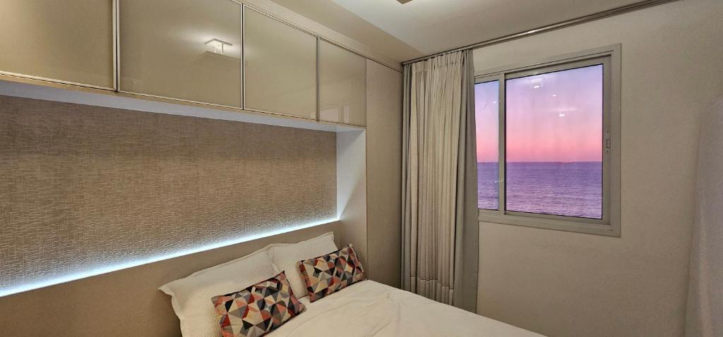 a bedroom with a bed and a window with the ocean at Vista para a Orla de VV in Vila Velha