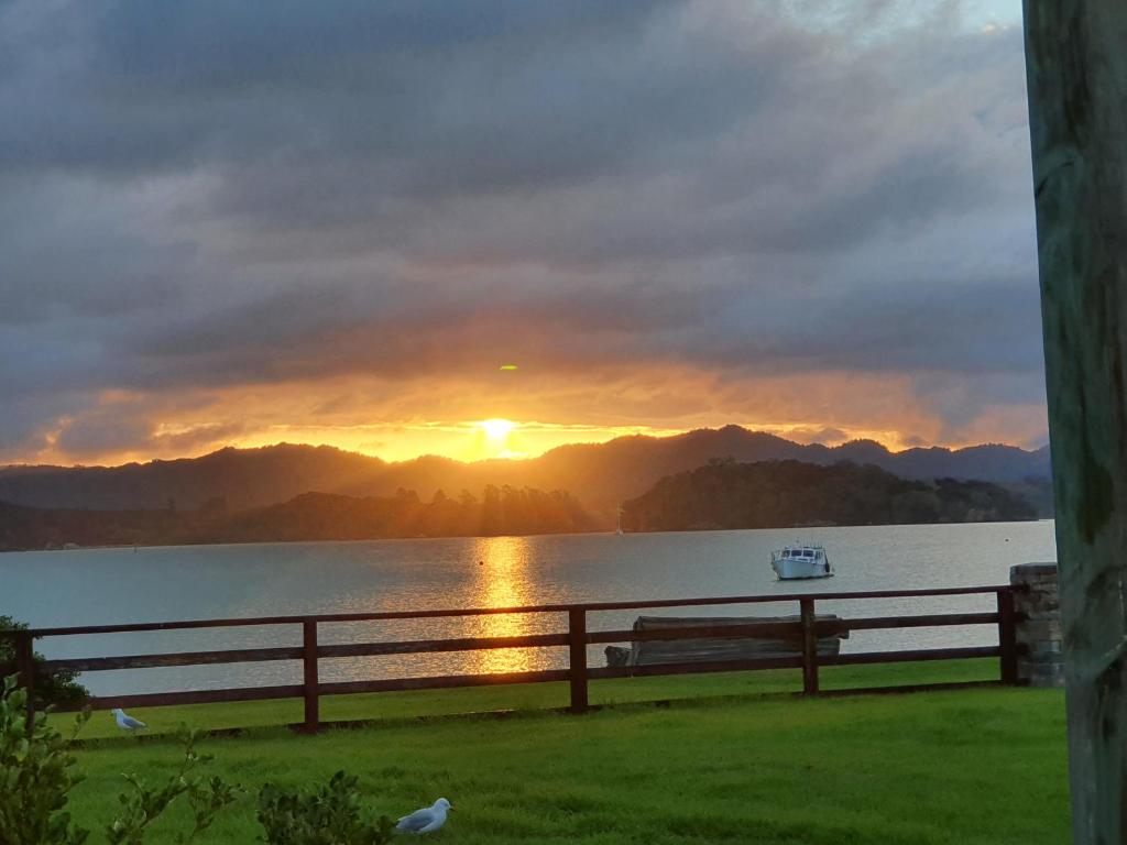 a sunset over a lake with a fence and a bench at Kirikiri Pawhaoa in Whangaruru