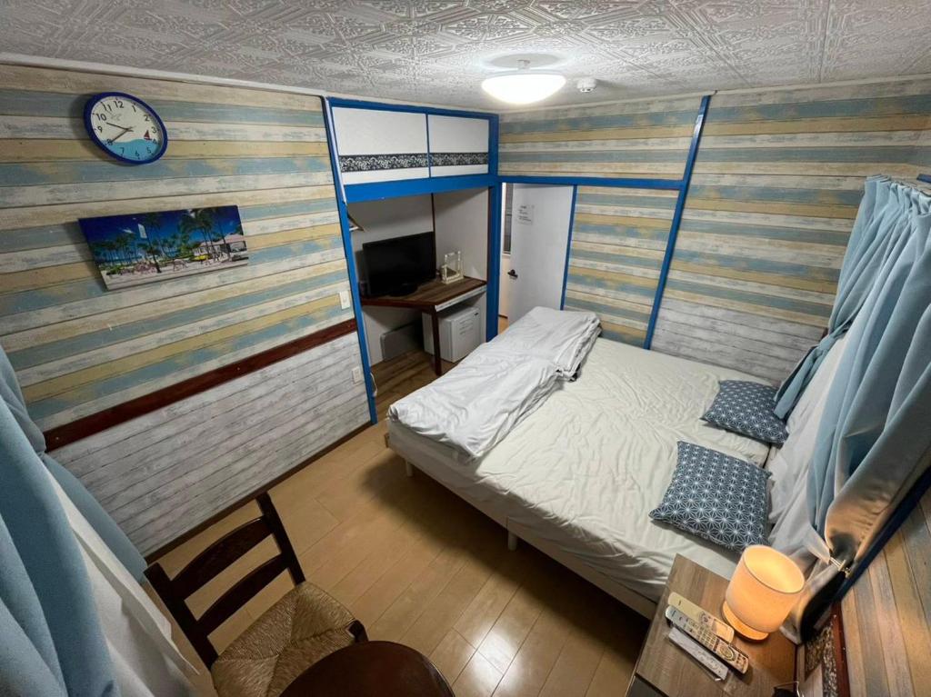 um pequeno quarto com uma cama e um relógio na parede em 宮古島ゲストハウス　マウイ em Arazato