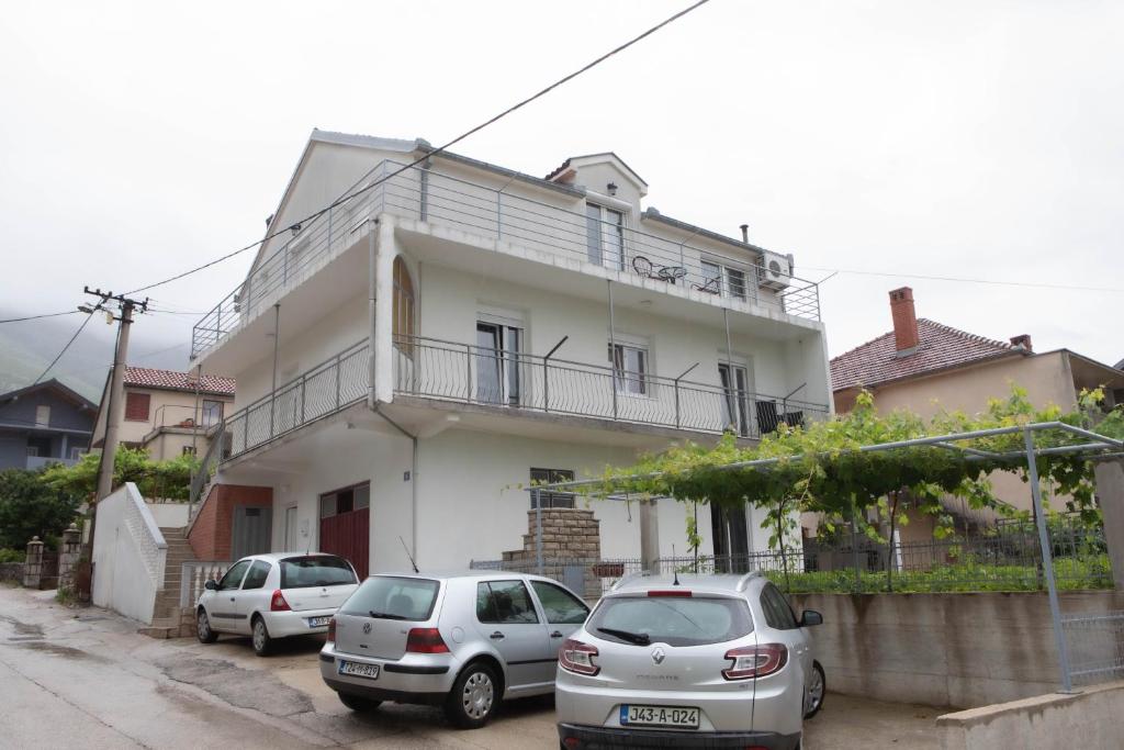 deux voitures garées devant une maison blanche dans l'établissement Apartmani Budimčić, à Trebinje