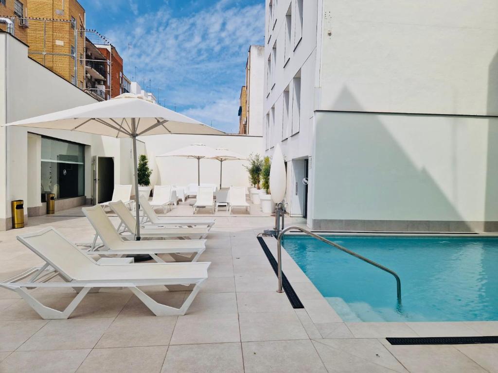 a pool with chairs and umbrellas next to a building at Virgen de los Reyes in Seville