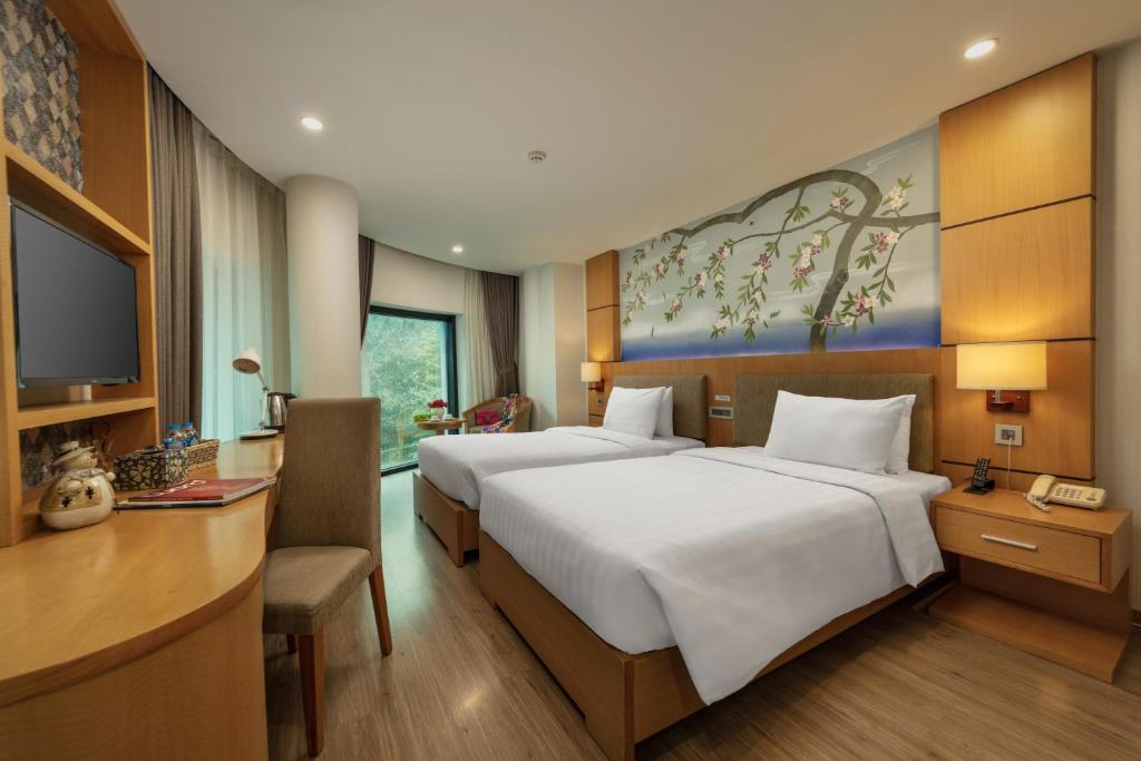 ハノイにあるHALO HANOI HOTELのベッド2台、デスク、テレビが備わるホテルルームです。