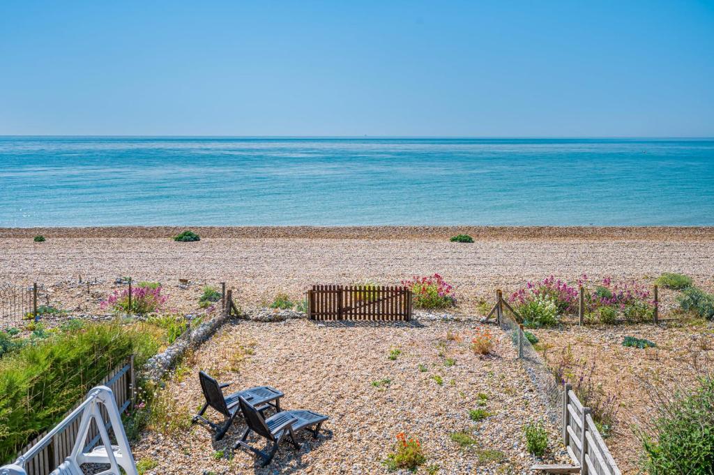 a beach with two chairs and flowers and the ocean at Pebble Paradise Beachfront Family Getaway in Pevensey