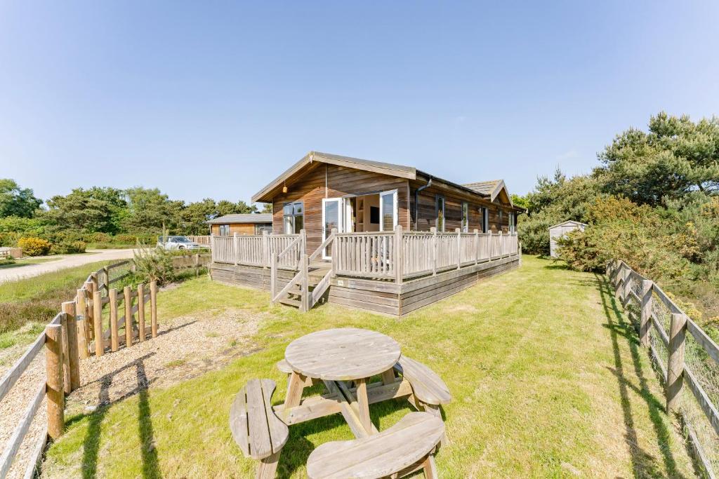 Cabaña de madera con mesa y valla en Heathland Lodge - Norfolk Cottage Agency, en Kelling