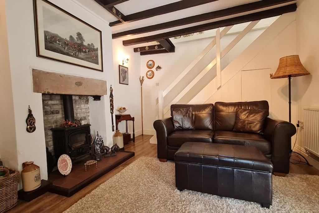 a living room with a leather couch and a fireplace at Peaceful cottage retreat in the Peak District in Wirksworth