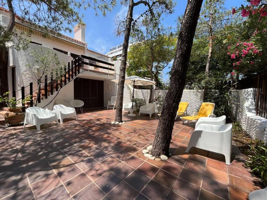 un patio con sillas blancas, mesas y árboles en Villa típica ideal para as suas férias em família! en Monte Gordo