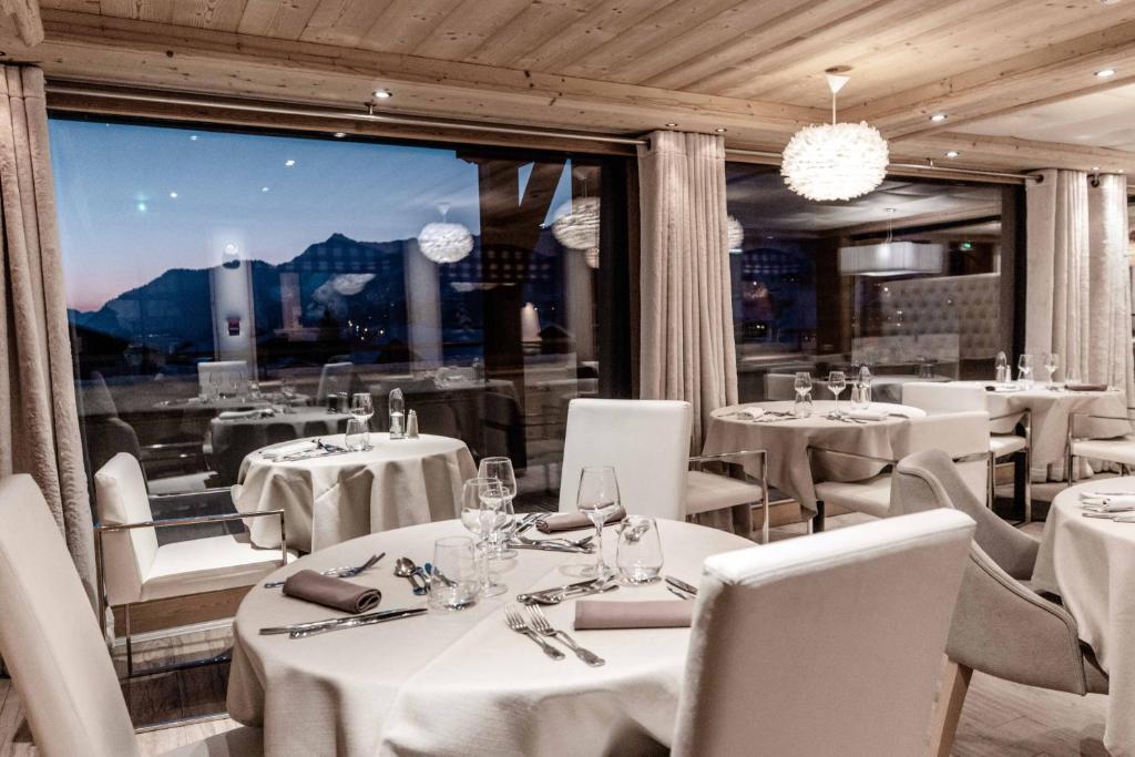 a restaurant with white tables and chairs and a large window at Hôtel Alpina &amp; SPA in Les Gets