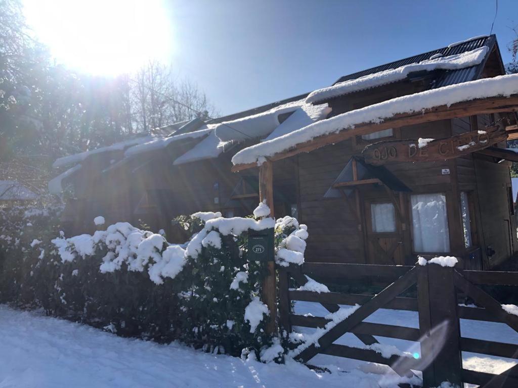 una cabaña con nieve en el techo y una valla en Cabañas Ojo de Cielo en San Carlos de Bariloche