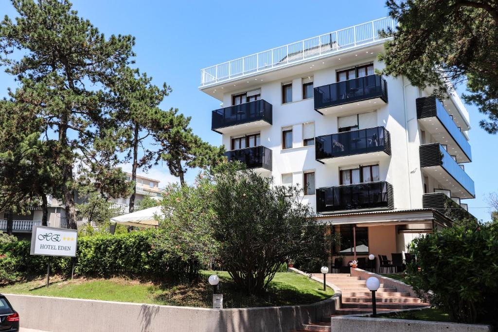 a white apartment building with balconies and trees at Hotel Eden in Lignano Sabbiadoro