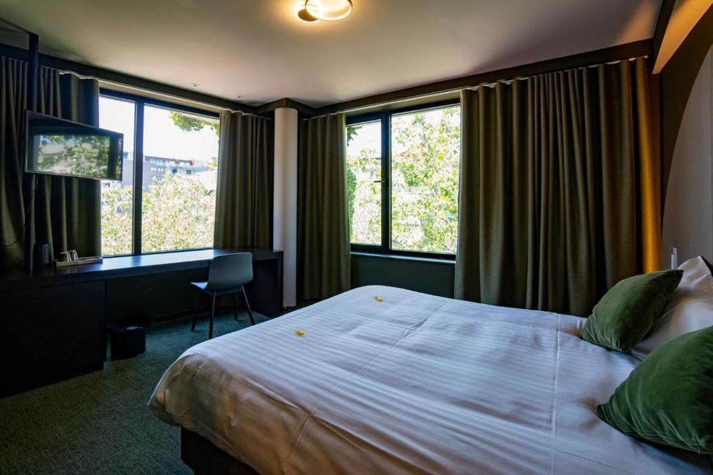 a bedroom with a bed and a desk and windows at Green Hotel in Genk