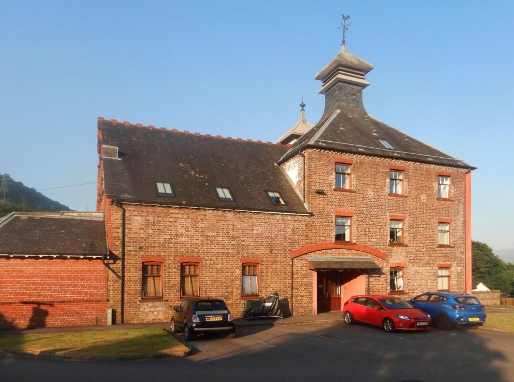 a large brick building with cars parked in front of it at Old Whisky Distillery Apartment in Fort William