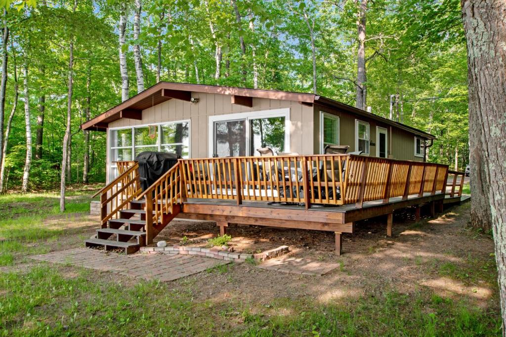 una pequeña casa en el bosque con una gran terraza en Behnkes Bungalow, en Manitowish Waters