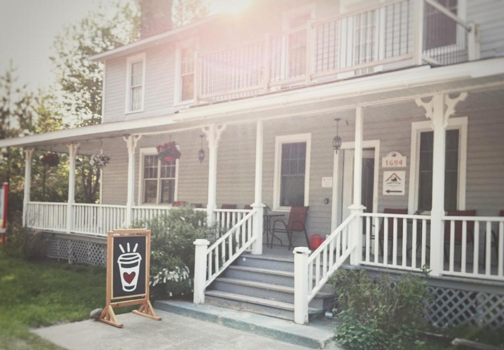 a white house with a porch and a sign on it at Auberge de la Gare, Station Soberlab in Sainte-Adèle