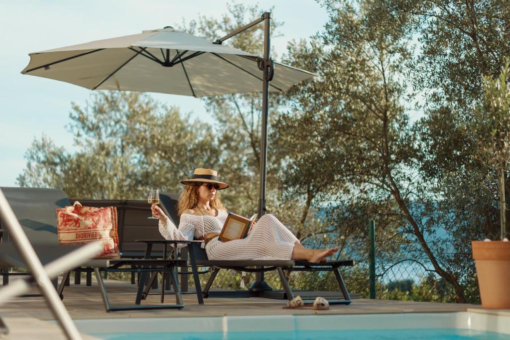 Una donna seduta su una sedia a leggere un libro vicino alla piscina di Aria di Mare Apartments a Tivat