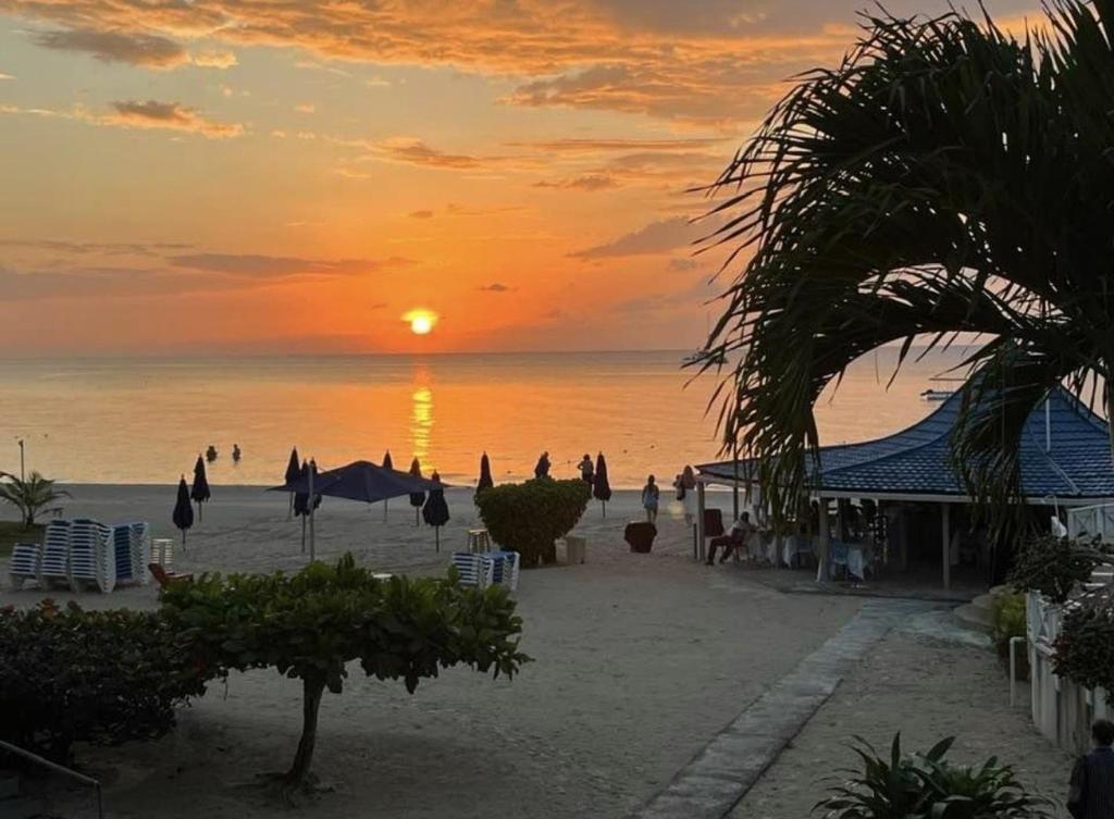 a sunset on a beach with chairs and umbrellas at Seacret Studios - Cozy Jamaican Retreat apts in Negril