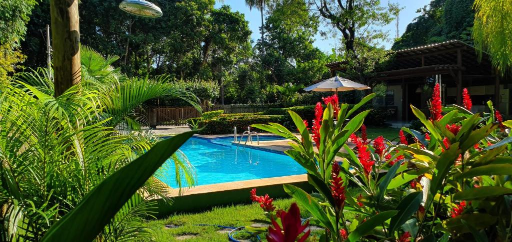 une piscine dans un jardin avec des fleurs rouges dans l'établissement Villa do Cajueiro - lofts com sala e cozinha, à Imbassaí