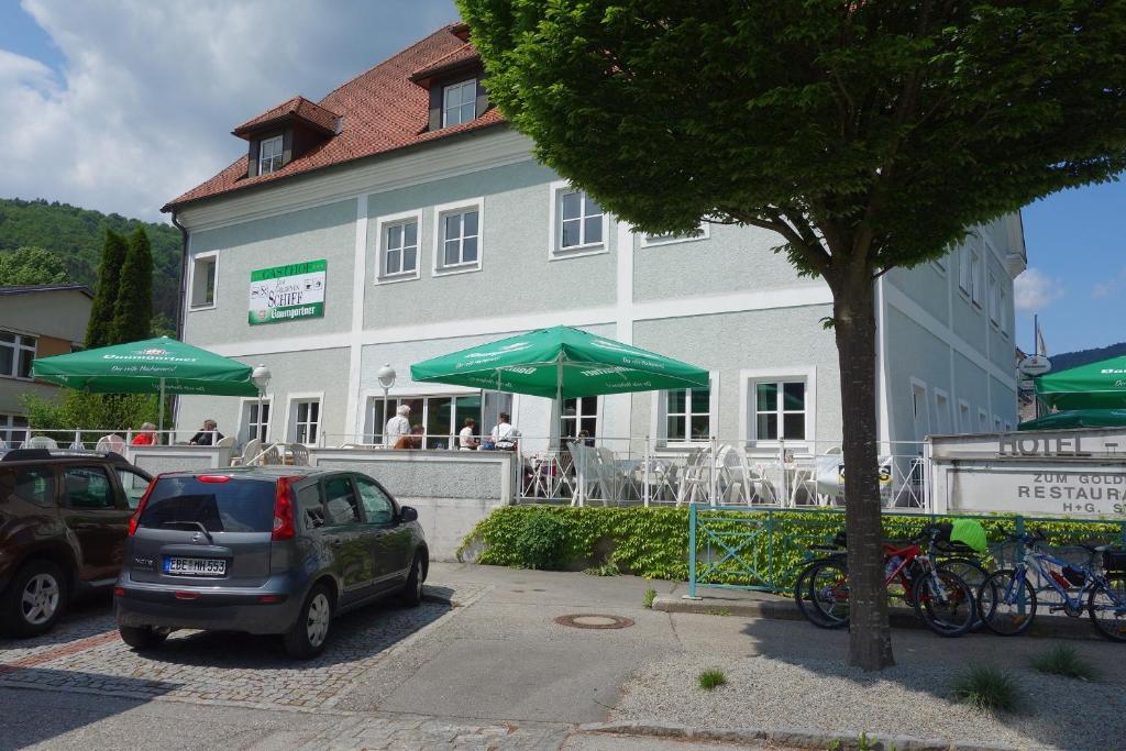 samochód zaparkowany przed budynkiem z zielonymi parasolami w obiekcie Goldenes Schiff Hotel-Mietparkplätze w mieście Engelhartszell