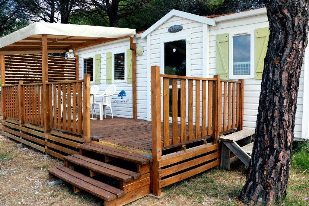 a cabin with a wooden deck next to a tree at Mobilhome «Perle marine»*6 personnes *3 Chambres*TV in Sigean