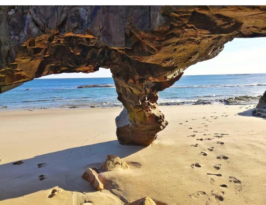 een rotsformatie op een strand met voetafdrukken in het zand bij Vistas al mar con jardín privado, piscina y padel in Foz