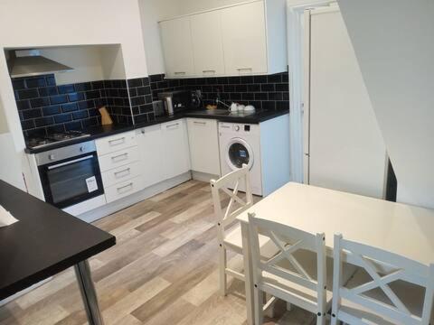 cocina con armarios blancos, mesa y lavadora en Double-bed (G2) close to Burnley city centre, en Burnley