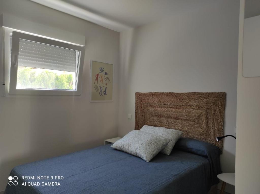 ein Schlafzimmer mit einem Bett mit einer blauen Decke und einem Fenster in der Unterkunft Casita moderna a escasos metros de Playa Terranova in Oliva