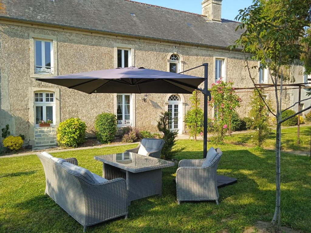 uma mesa e cadeiras com um guarda-sol em frente a uma casa em Aux Léopards Normands em Mandeville-en-Bessin
