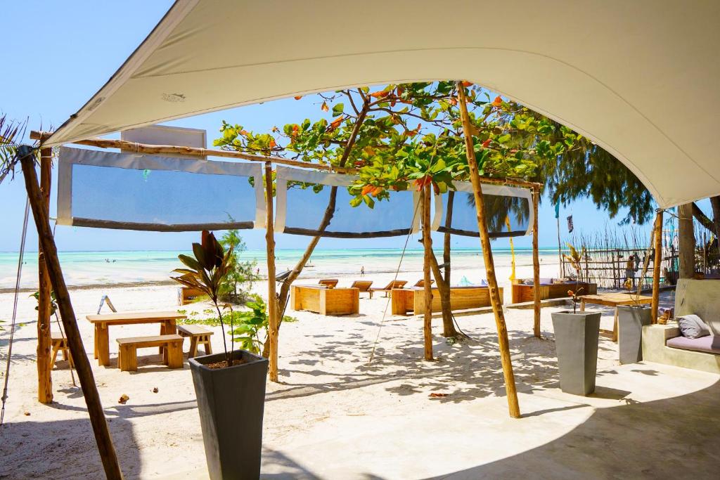 een tent op het strand met stoelen en bomen bij Meraki - Cafe Bar Rooms in Paje