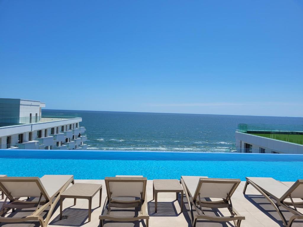 Japandi Queen Std - Infinity Pool & Spa Resort في مامايا نورد نافورداي: حمام سباحة مع الكراسي والمحيط في الخلفية