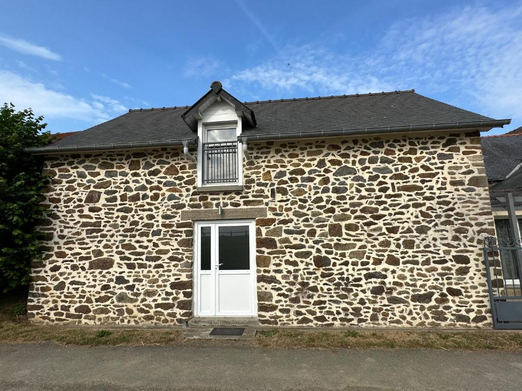 a stone building with a white door and a window at La maison du Chêne 1 in Miniac-Morvan