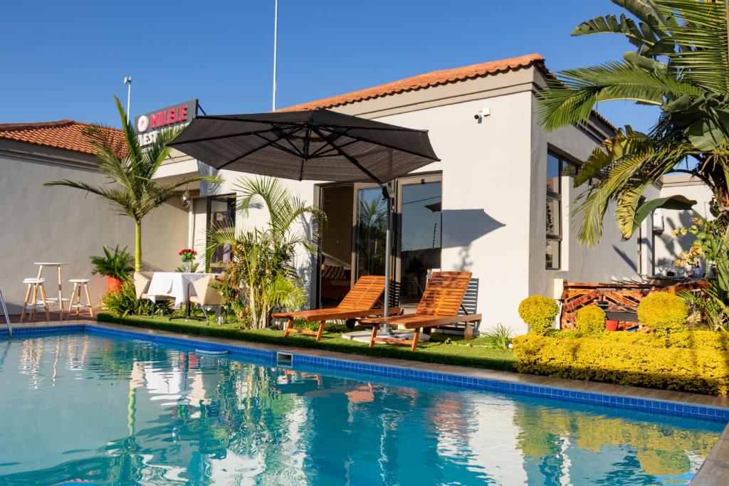 a swimming pool in front of a house with an umbrella at Milele Lodge in Gaborone