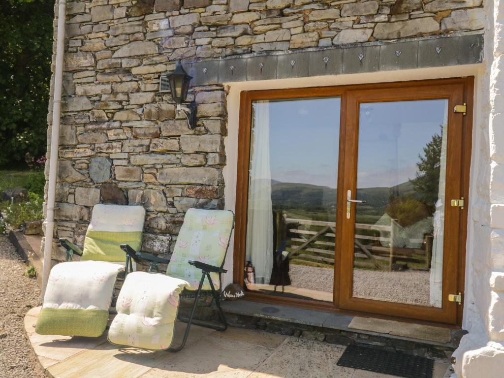 two chairs sitting next to a stone building with a sliding glass door at Wren's Nest in Keswick