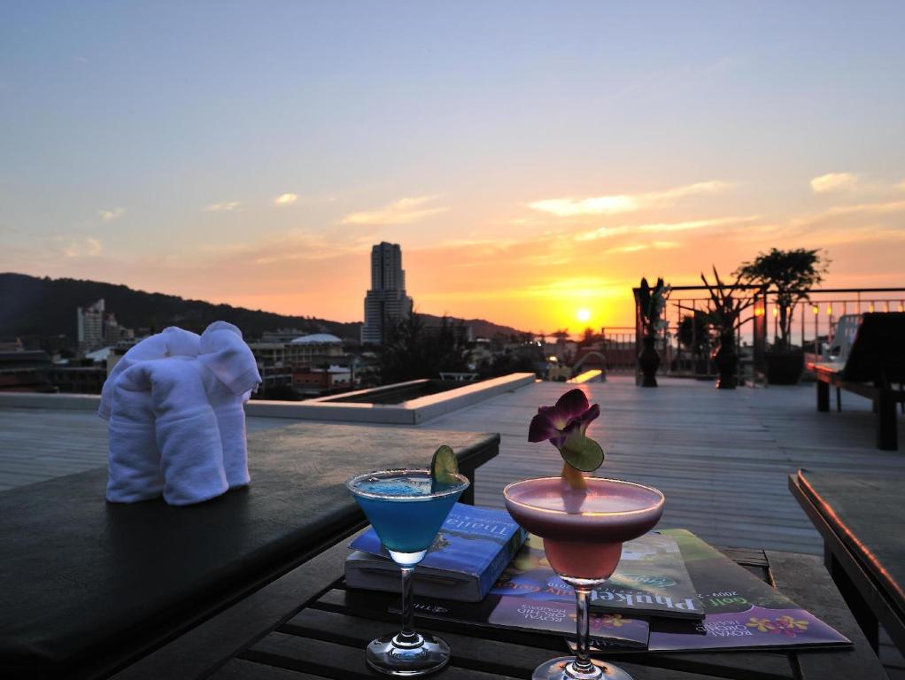 a table with two drinks on a balcony with the sunset at Cocoon APK Resort & Spa in Patong Beach