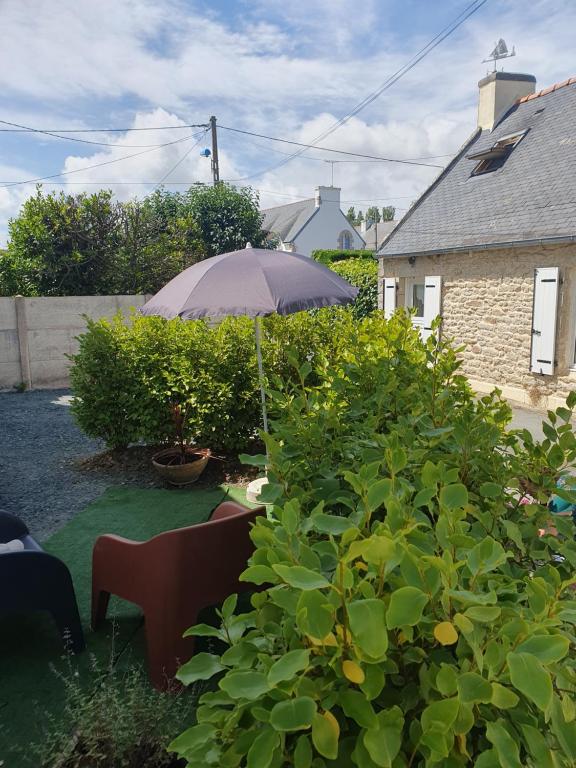 a garden with an umbrella and chairs and bushes at penty vero in Plobannalec-Lesconil
