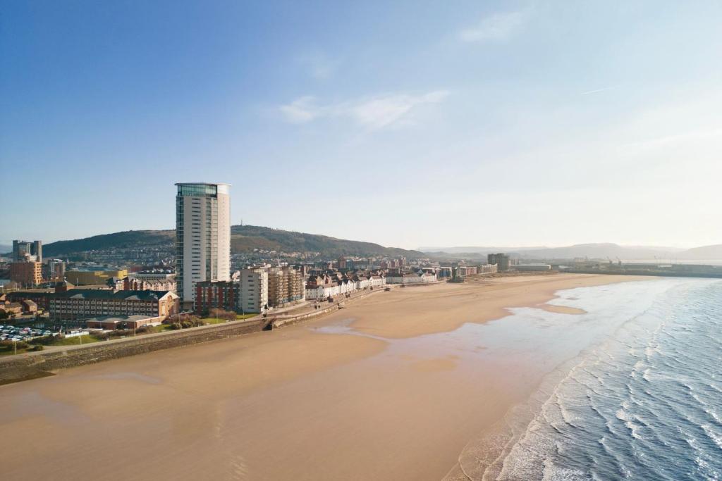 Blick auf einen Strand mit Gebäuden und das Meer in der Unterkunft Delta Hotels by Marriott Swansea in Swansea