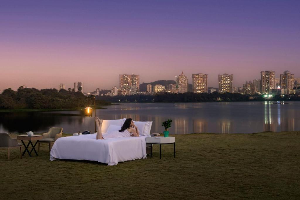 eine Frau, die in einem Bett mit Blick auf eine Stadt liegt in der Unterkunft The Westin Mumbai Powai Lake in Mumbai