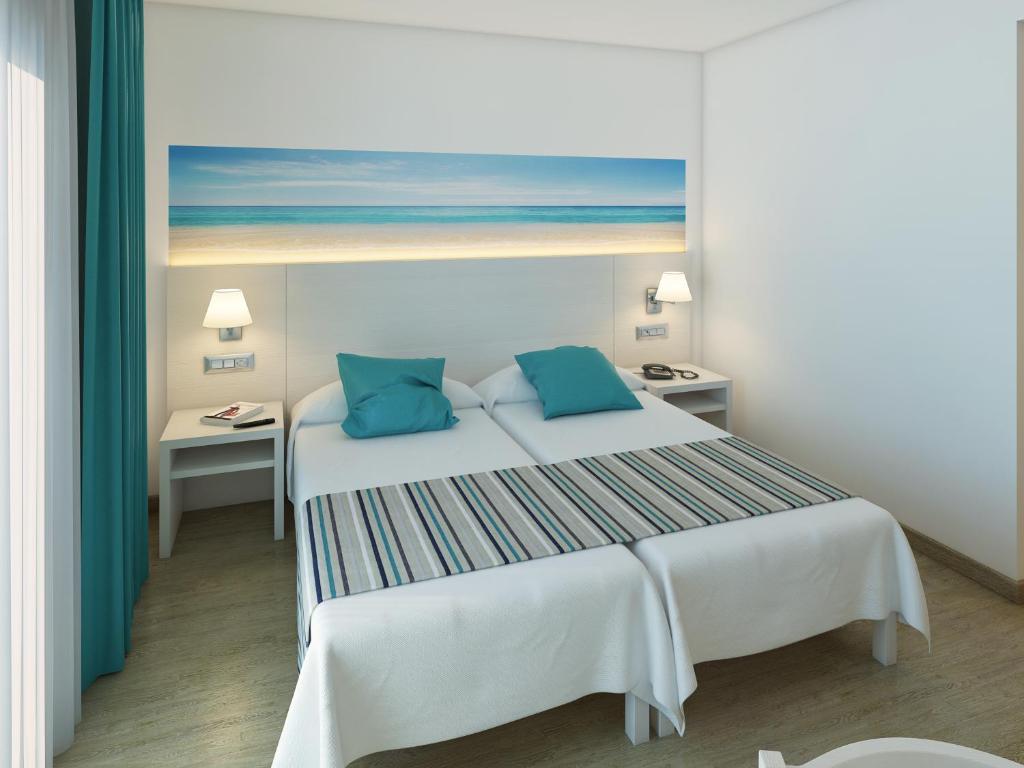 a bedroom with a large white bed with blue pillows at Hotel Playas de Paguera in Paguera