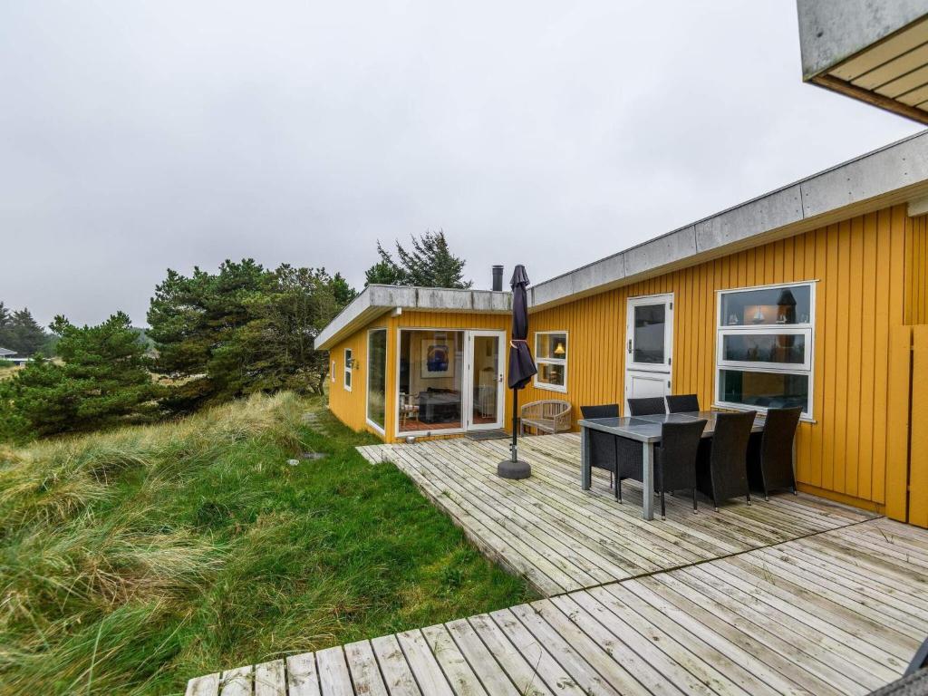 een klein geel huis met een houten terras bij Holiday home Henne XII in Henne Strand