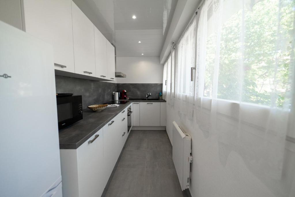 a kitchen with white cabinets and a large window at Les cerisiers un petit coin de paradis pour deux proche du lac! in Sévrier