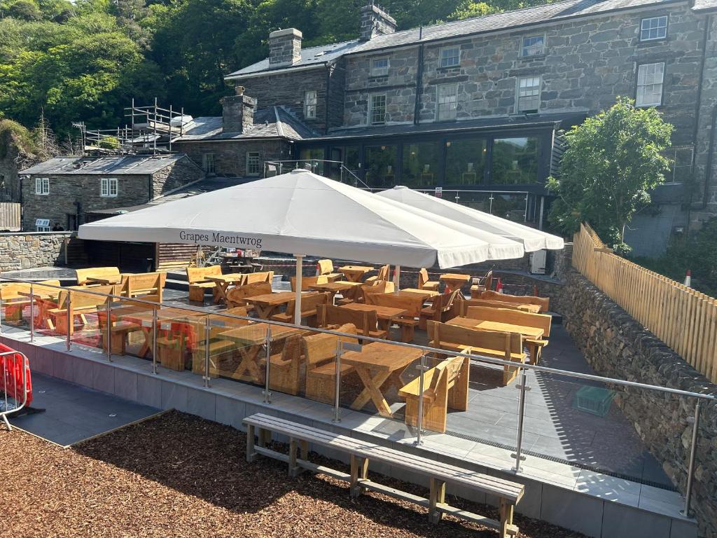 een restaurant met houten tafels en een witte parasol bij Grapes Hotel, Bar & Restaurant Snowdonia Nr Zip World in Blaenau-Ffestiniog