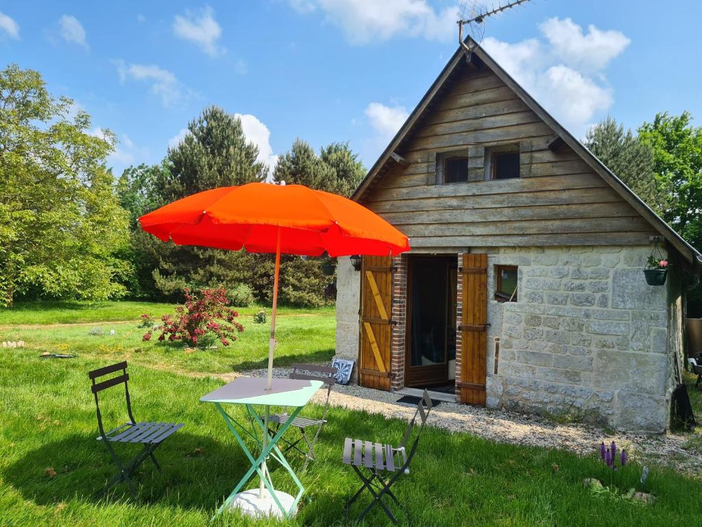 une table avec un parapluie orange devant un bâtiment dans l'établissement Petite Maison de campagne, à Fauguernon