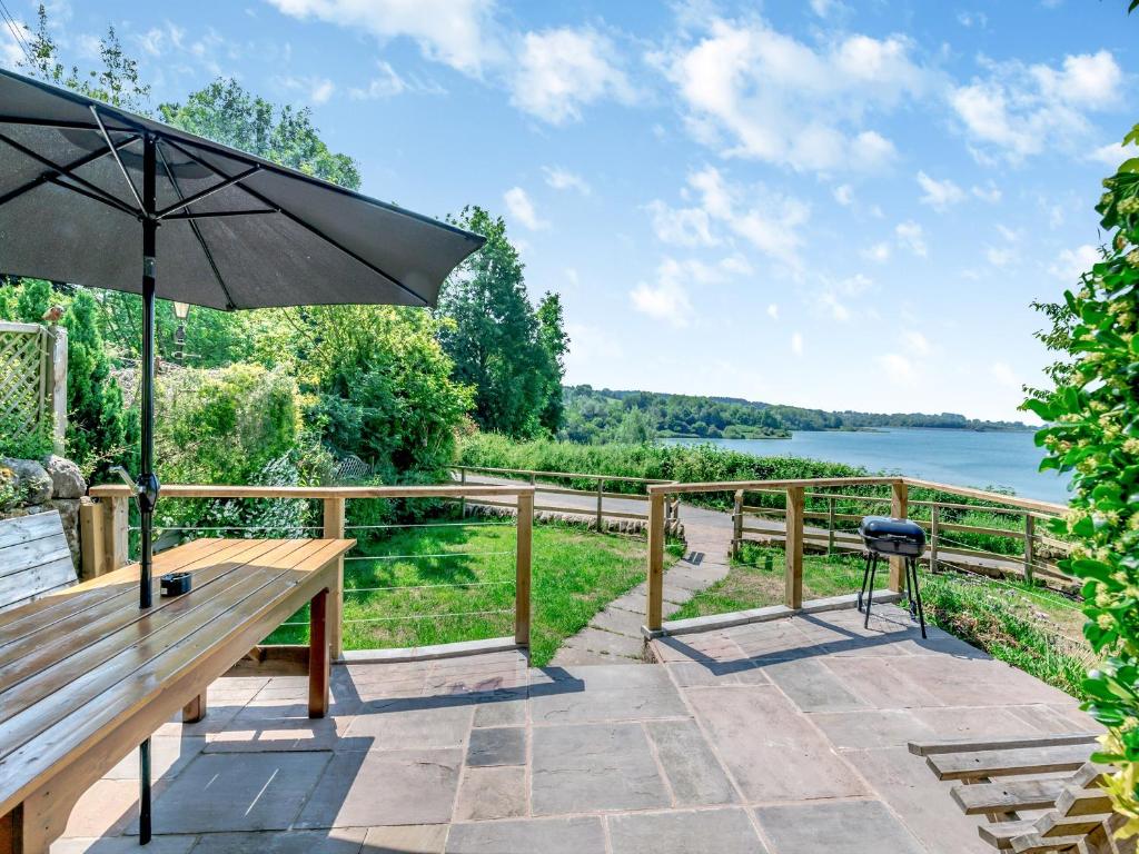 a wooden bench with an umbrella overlooking a lake at Kingfisher Barn - Uk44098 in Carsington