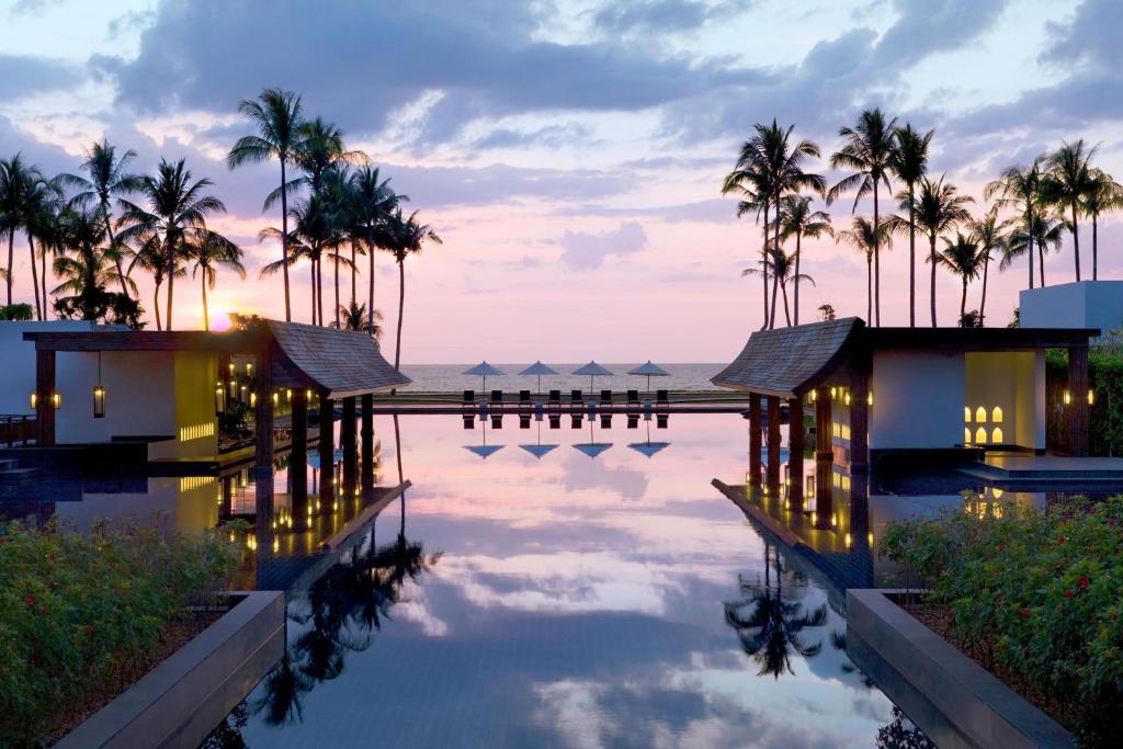 ein Resortpool mit Palmen und dem Meer in der Unterkunft JW Marriott Khao Lak Resort Suites in Khao Lak