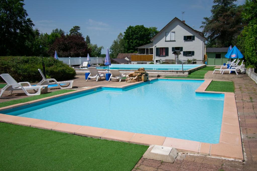 a swimming pool with chairs and a house in the background at Camping des Bains in Saint-Honoré-les-Bains